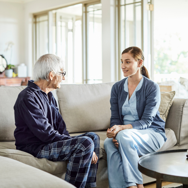 an elderly man sitting in his living room with an in home nurse talking