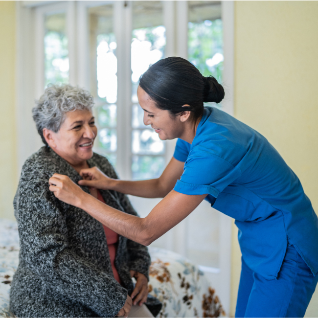 nurse helping elderly woman put on a cardigan